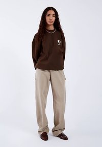 Brun sweatshirt med et grafisk hjerte-design, kombineret med lyse beige bukser med vide ben og mørkebrune loafers. Enkel, afslappet pasform.