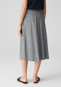 Knielanger, grauer Rock mit strukturiertem Muster, elastischem Bund und Seitentaschen. Kombiniert mit schwarzen Riemchen-Sandalen.