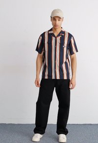 Cămașă cu mânecă scurtă, cu dungi în culorile navy, alb și portocaliu, având două buzunare în față; asortată cu pantaloni negri și adidași albi.