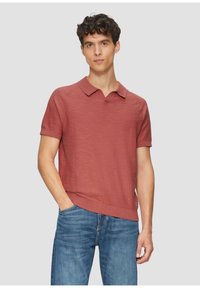 Kurzarm-Polohemd in gedämpftem Rostrot mit strukturiertem Gewebe, einem Kragen und geripptem Saum. Kombiniert mit mittelblauer Denim-Jeans.