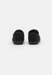 Černé plátěné slip-on boty s nízkým profilem, polstrovaným límcem a gumovou podrážkou. Texturovaný svršek s akcenty švů.