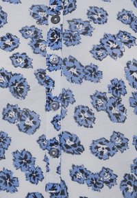 Leichtes Stoffoberteil mit floralem Muster in Blau- und Schwarztönen, mit einer Knopfleiste und fünf Knöpfen entlang der Mitte.