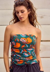 Haut sans bretelles vert avec un motif de fruits éclatant en orange, rose et bleu. Présente des fronces sur les côtés et des liens, fabriqué en tissu doux et texturé.