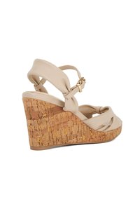 Sandale beige à talon compensé en liège, avec des sangles en cuir nouées, une bride à la cheville avec une boucle en or, et une surface texturée en liège.