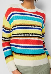 Monivärinen villapaita, jossa on tekstuuriset raidat punaisessa, sinisessä, turkoosissa, keltaisessa ja mustassa. Suunniteltu pyöreällä kauluksella ja ribbaus-hihoilla.