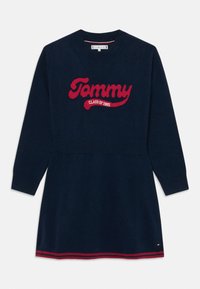 Marinblå stickad klänning med långa ärmar och ribbade muddarna, utrustad med en röd "Tommy CLASS OF 1985" logotyp och en randig fåll.