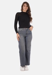 Maglietta nera a coste con maniche lunghe e collo alto, abbinata a jeans denim chiari, a taglio loose fit e sneakers bianche.