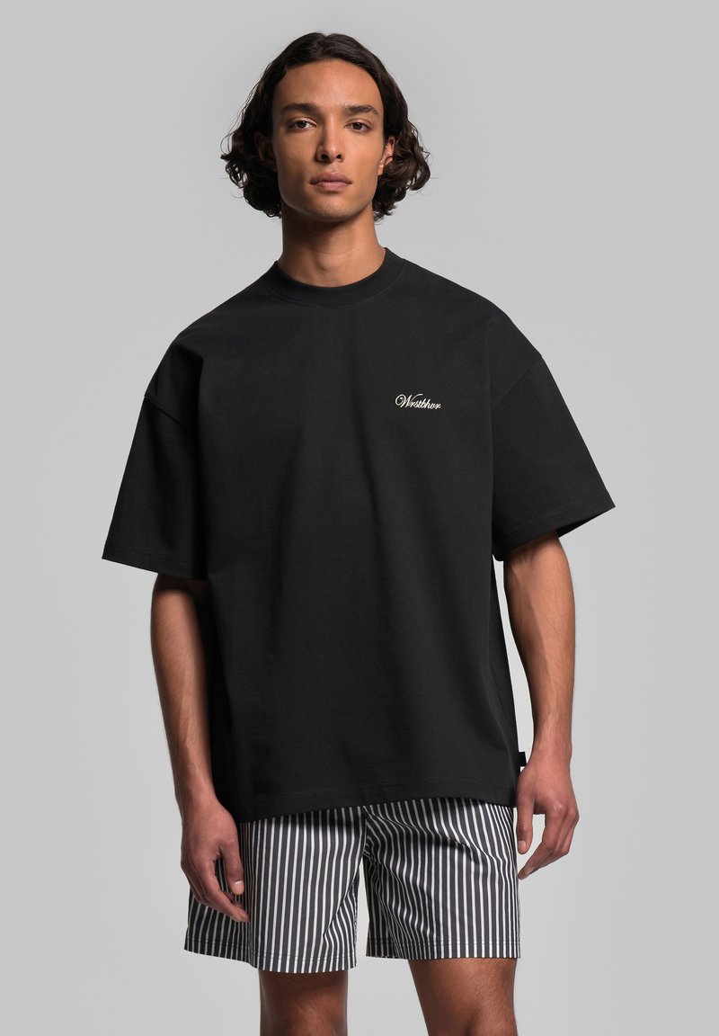 Svart bomull T-shirt med korta ärmar och rund halsringning, med vit broderad text på bröstet. Matchad med randiga shorts.