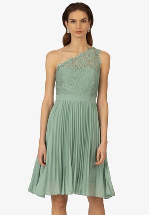 Robe vert menthe à une épaule avec un corsage en dentelle, une jupe plissée et une taille ajustée. Conception simple avec des accents texturés.