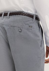 Grau gemusterte Hose aus strukturiertem Stoff, mit einem geflochtenen braunen Gürtel, Knopfverschluss und seitlichen Taschen.