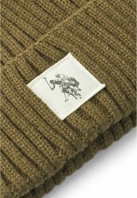 Berretto lavorato a maglia verde oliva con texture a coste e una toppa quadrata con una grafica di un cavallo e cavalieri in nero su sfondo bianco.