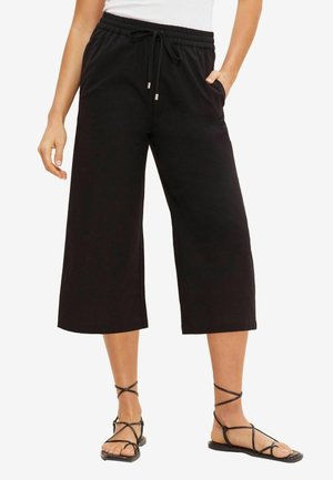 Zwarte, cropped sweatpants met een elastische tailleband en een trekkoord; voorzien van zijzakken en een relaxed fit. Gecombineerd met zwarte, verstelbare sandalen.