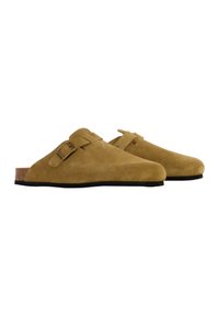 Mules en suède, couleur beige, avec une semelle en liège, une semelle en caoutchouc noir et une bride réglable sur le côté.