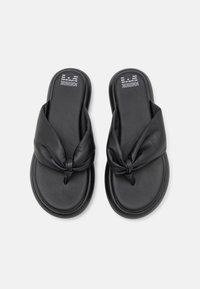 Sandales à glissière en cuir noir avec un design de lanière nouée. Texture lisse avec une semelle rembourrée, adaptées pour une utilisation décontractée.