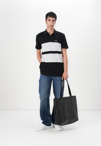 Svart og hvit stripete polo skjorte, kort erm, med logo. Båret med blå jeans og en svart totebag. Hvite sneakers fullfører antrekket.