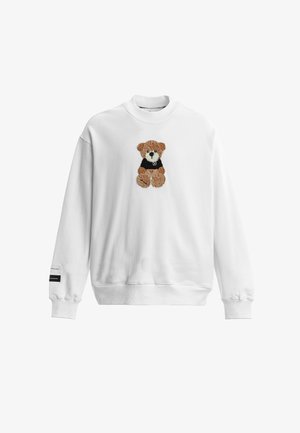 Sudadera blanca de manga larga con un osito de peluche marrón con una camiseta negra bordada en el pecho y una pequeña etiqueta en el puño izquierdo.