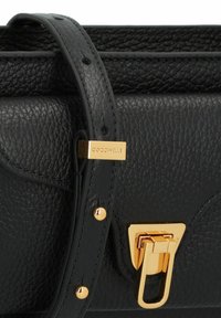 Bolso de mano de cuero negro con textura granulada, herrajes dorados, un cierre triangular y una correa con etiqueta de la marca.