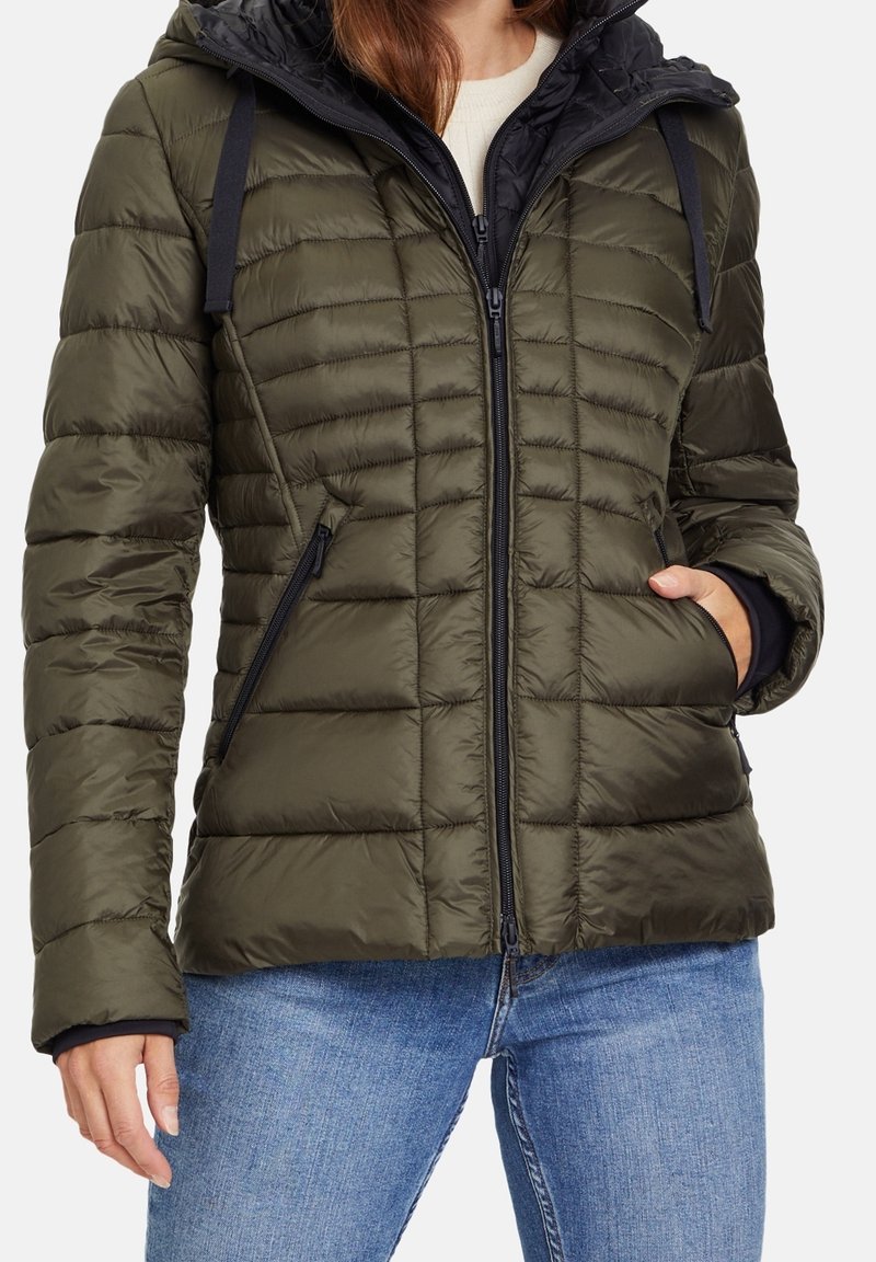 Veste matelassée vert olive gonflée avec fermeture éclair, texture matelassée, deux poches latérales et une capuche doublée noire. Comprend des cordons de serrage noirs et des accents noirs.