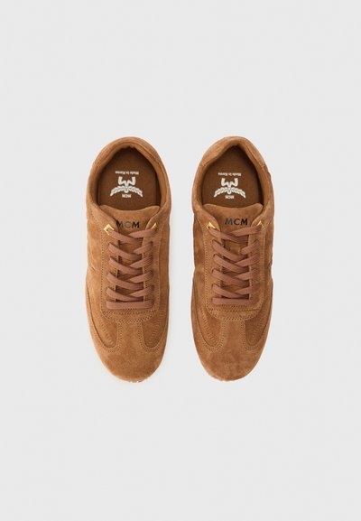 Baskets en suede marron avec des orteils ronds, des accents cousus et des lacets marron. Elles présentent un logo sur la languette et des semelles en caoutchouc texturé.