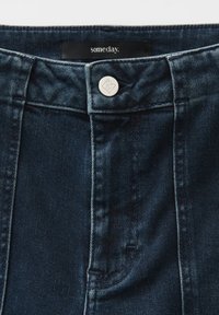Donkerblauwe denim jeans met witte knoopsluiting, met een gestikte tailleband en merketiket "someday." Gestructureerde stof met lichte vervaging.