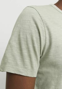 Lys grøn kortærmet t-shirt lavet af blød,tekstureret stof. Har en rund halsudskæring og synlige sømme langs ærmerne og kanten.