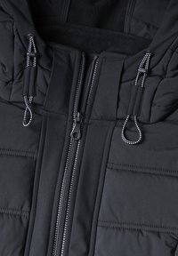 Close-up of black padded jacket with central zipper and adjustable hood cords with black and white loops.