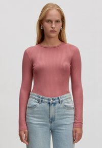 Langärmliges, geripptes Oberteil aus weichem rosa Stoff, mit rundem Ausschnitt und figurbetonter Silhouette, kombiniert mit hellblauen hochgeschnittenen Jeans.
