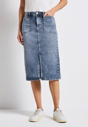 Denim rok, lichtblauw, van gemiddelde lengte met een voorknipt, twee voorkcontainers en metalen knoopsluiting. Gecombineerd met witte sneakers.