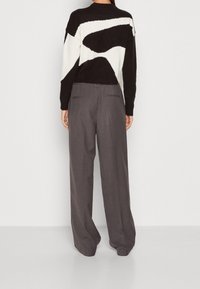 Svartvit mönstrad tröja med en fuzzy textur, tillsammans med grå vida byxor med bakfickor och skräddarsydd passform.