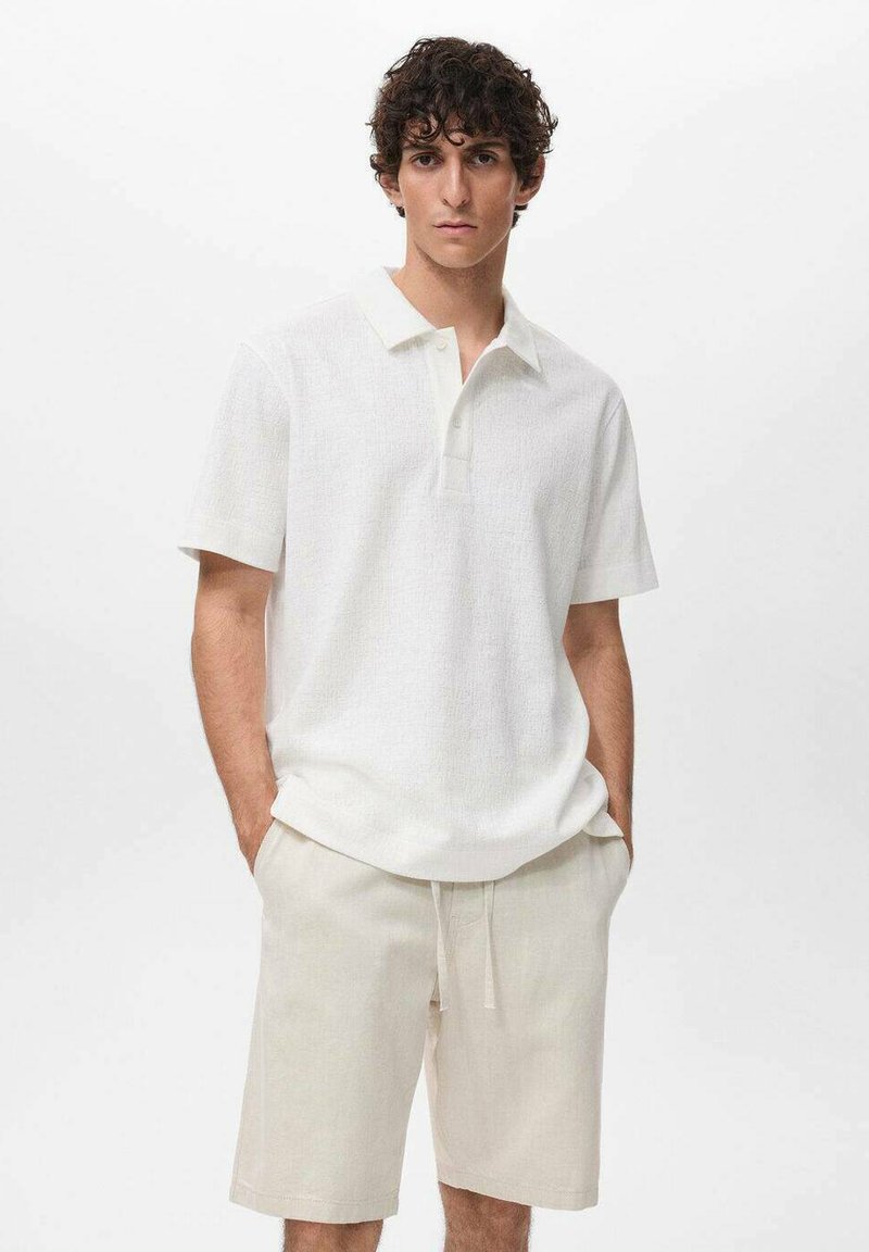 Hvid tekstureret polo-shirt med krave, parret med cremefarvede shorts. Begge beklædningsgenstande har en afslappet pasform og blødt stof.