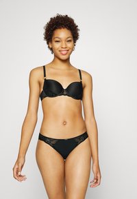 Ensemble de lingerie noire comprenant un soutien-gorge moulé avec des accents en dentelle et des bretelles ajustables, associé à un string à bord dentelé assorti.