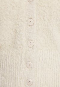 Button-up cardigan made of soft, fluffy cream-colored material with horizontal ribbing and six light-colored buttons down the front.