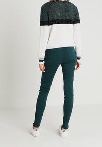 Suéter de punto con rayas horizontales en verde oscuro, negro y blanco; combinado con jeans ajustados en verde azulado; llevado con zapatillas blancas.