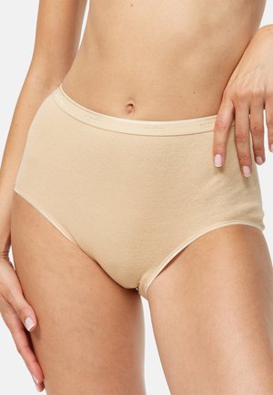 Culotte beige taille haute sans coutures portée par une personne les mains posées sur les hanches, montrant le milieu du corps et le haut des cuisses.