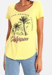 Gul kortärmad T-shirt med rund halsringning, prydd med palmträdsgrafik och texten "California" i rosa. Mjuk tyg med en avslappnad passform.