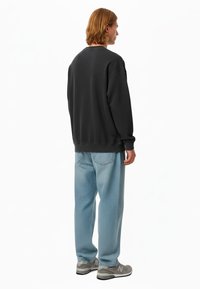 Felpa grigia con maniche lunghe e polsini a costine, abbinata a jeans blu chiaro. Sneakers grigie con suola in gomma completano l'outfit.