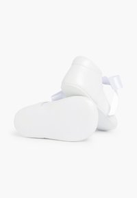 Zapatos de bebé de cuero blanco con suela blanda, punta redondeada y acento de lazo de satén en el talón, que cuentan con una textura suave y un diseño minimalista.