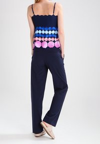 Námořnická bezramínková halenka s gradientním šestiúhelníkovým vzorem v modré, tyrkysové a růžové; spárovaná s námořnickými kalhotami širokého střihu a světlými balerínami.