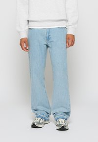 Light blue denim jeans with a relaxed fit, featuring a classic five-pocket design and subtle fading. Worn with a gray sweatshirt and sneakers.