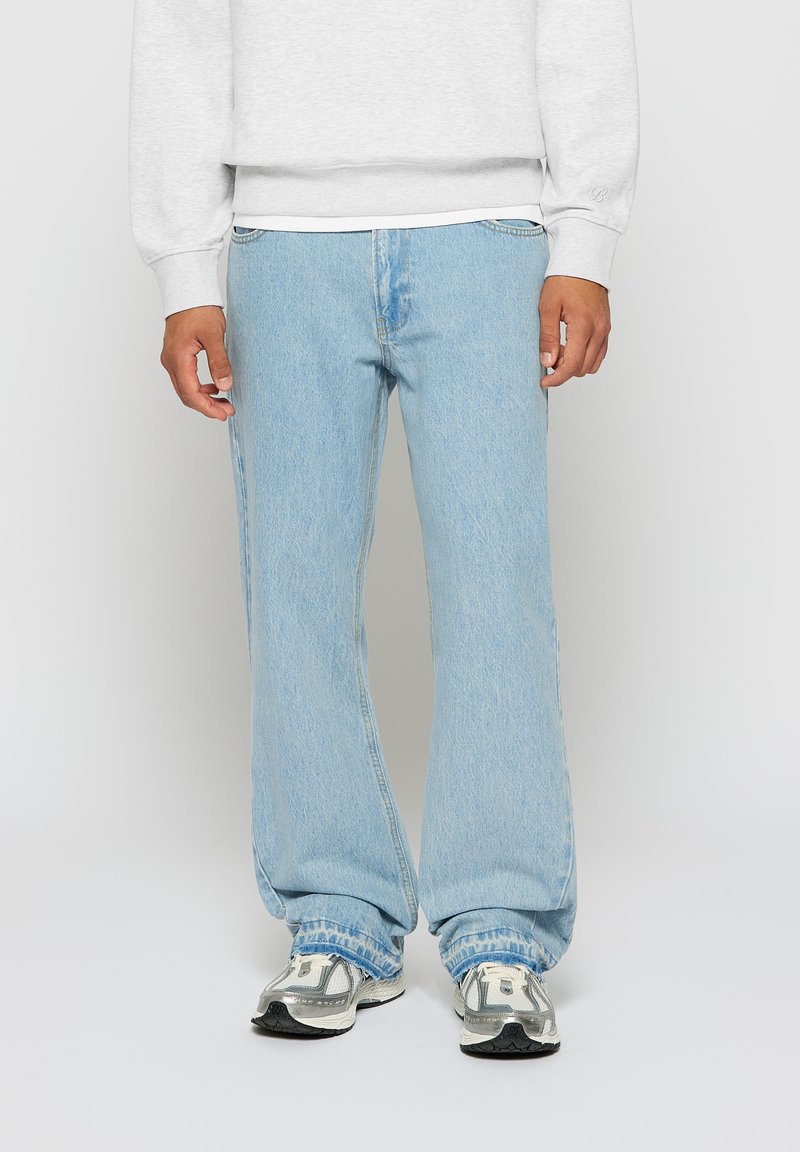 Light blue denim jeans with a relaxed fit, featuring a classic five-pocket design and subtle fading. Worn with a gray sweatshirt and sneakers.