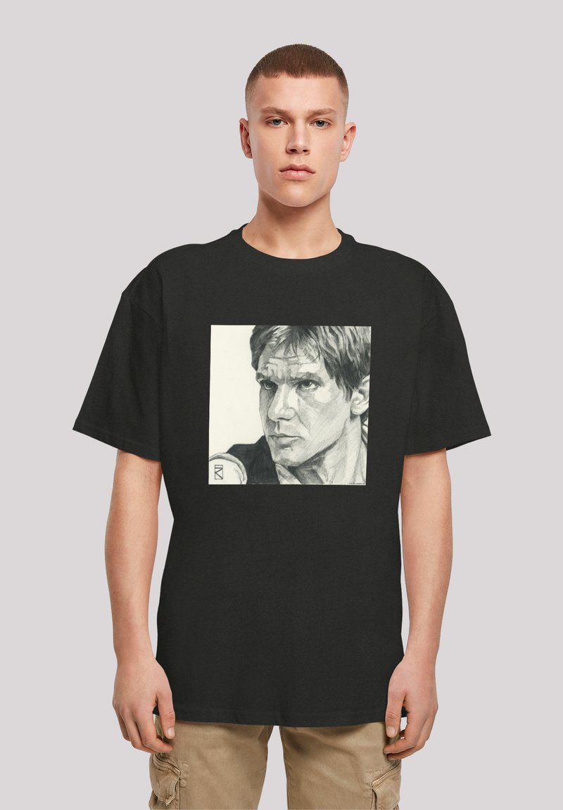 Sort t-shirt med et firkantet grafisk print af en blyantsketch af en mands ansigt, detaljeret udtryk og tekstureret hår, centreret på brystet.