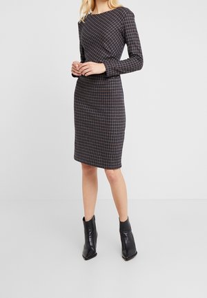 Jurk met lange mouwen, nauwsluitend, gemaakt van donkere stof met een geruit patroon in beige en donkerblauw. Gestyled met zwarte enkellaarsjes met puntige neus.