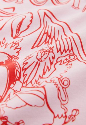 Biały materiał z czerwonym nadrukiem przedstawiającym lwa, skrzydła i inne misternie wykonane detale. Faktura wydaje się gładka i miękka.