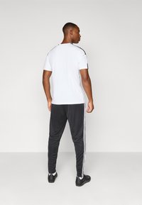 Hvit t-skjorte med korte ermer og svarte detaljer, kombinert med svarte joggebukser med hvite sidestiper, laget av et glatt og lett materiale.