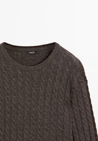 Pull gris foncé à col rond en maille torsadée avec manches longues et étiquette de marque visible à l'encolure.