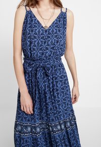 Robe bleue à imprimé floral avec un décolleté en V, des bretelles réglables, une taille cintrée et une jupe à volants avec un ourlet à motifs et des accents scintillants.