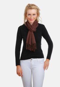 Écharpe marron en tissu doux, drapée autour du cou. Bords effilochés. Portée sur un haut noir et un pantalon blanc. Fond uni.