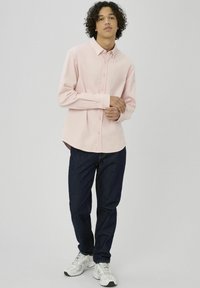 Chemise rose clair à boutons avec col, associée à un jean bleu foncé et des baskets grises. La chemise présente des rayures verticales.