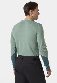 Dlouhý rukáv košile v světle zelené barvě s modrými akcenty a texturovanou tkaninou. Obsahuje zesílené švy podél švů a kulatý výstřih.