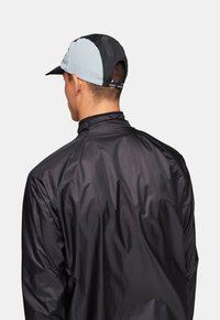 Svart lättviktig löparjacka med hög krage, bärs över en grå och svart löparkeps med en texturerad design och böjd skärm.